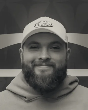 Black-and-white portrait of Noah Armstrong, bearded and smiling, in a white cap.